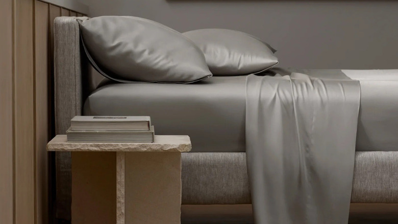 Light grey bamboo sheets on a bed with a side table and decor items in the foreground