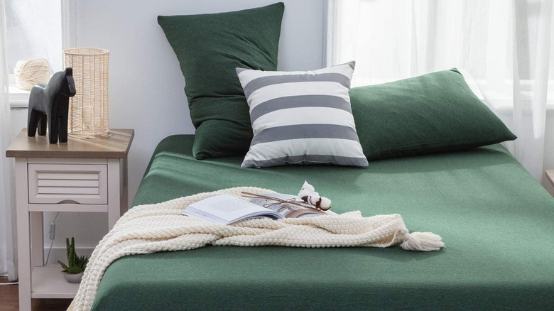 Green jersey sheets on a bed with a cream throw and striped pillow along with decorations in background