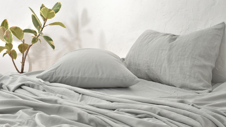 Grey linen sheets on a bed with a plant in the background
