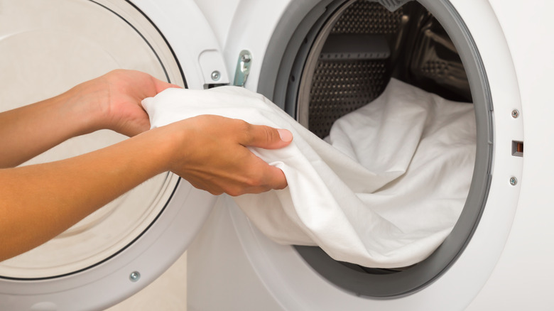 Pair of hands pulling white sheets from a front loading washing machine