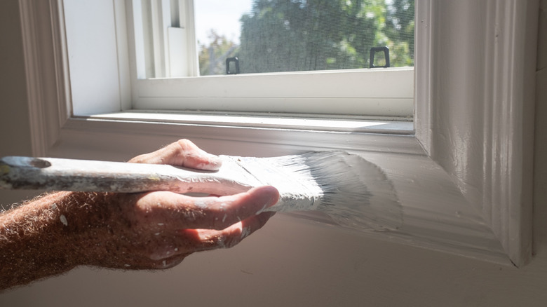 Close-up of a painter painting a window trim with a large angled sash brush