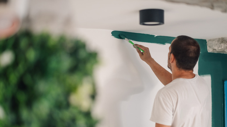 A main painting a the seam between a wall and a ceiling in a house