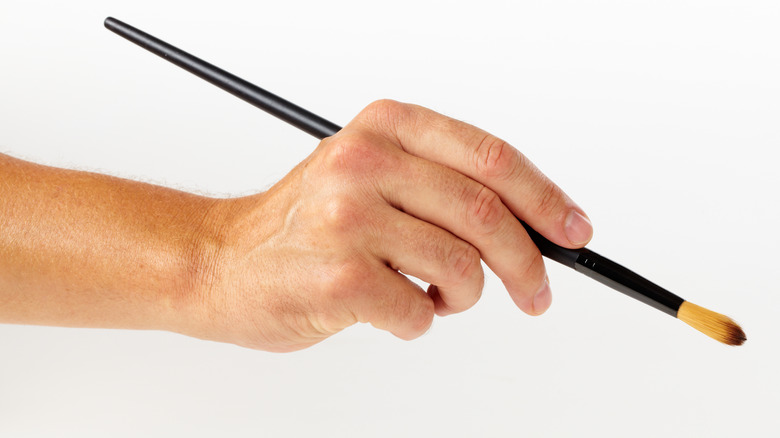 A hand holding a round paintbrush