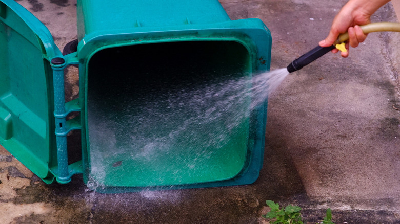 A homeowner cleaning a green garbage can