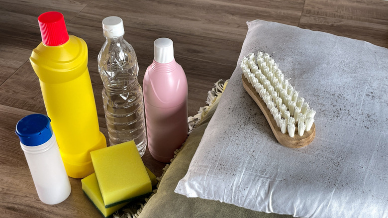 A moldy pillow with bottles of cleaner, two sponges, and a brush