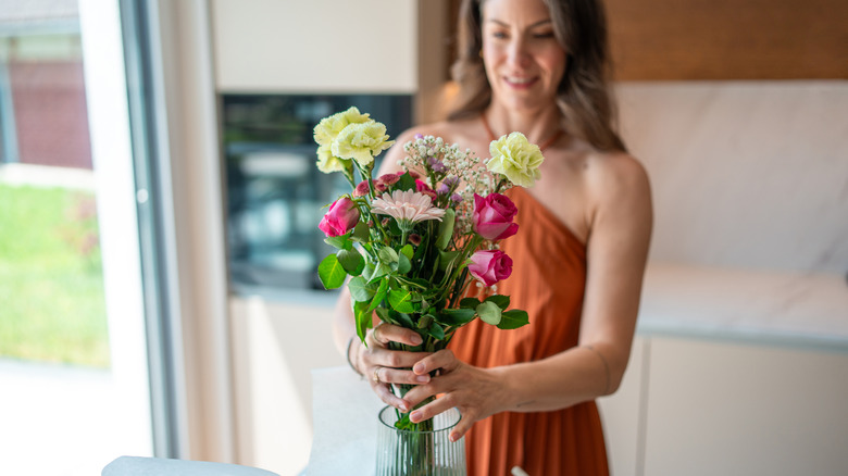 A woman placing cut flowers in a vase