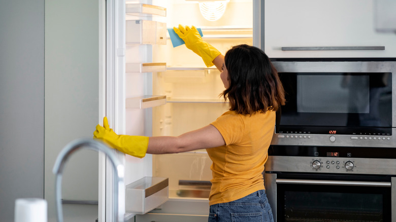 A young woman cleaning a fridge