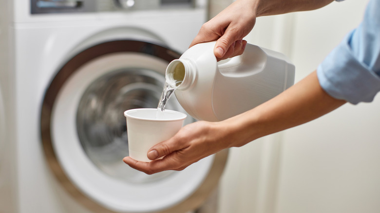 Close up of hands pouring bleach with a washing machine in the background