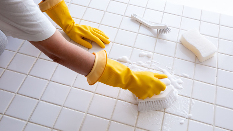 Close up of gloved hands scrubbing tiles with a brush