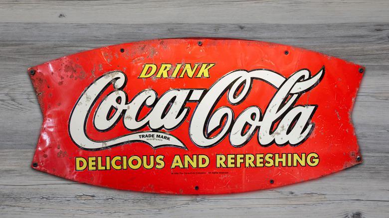 An old Coca Cola metal sign against a wood wall.