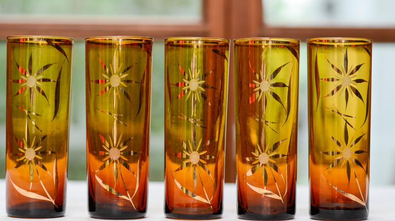 Five amber-colored glasses standing in a row next to each other in front of a window