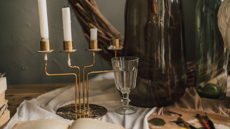 A vintage copper candle holder with partially melted candles on top and glasses around it
