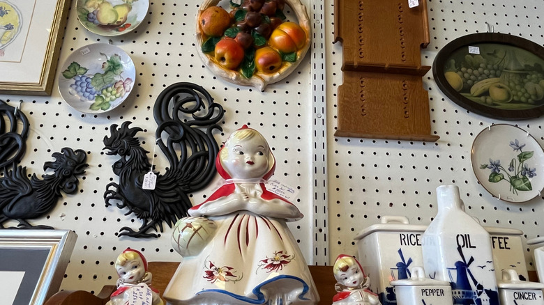 A thrift store wall with various dolls, containers, plates, and decorations