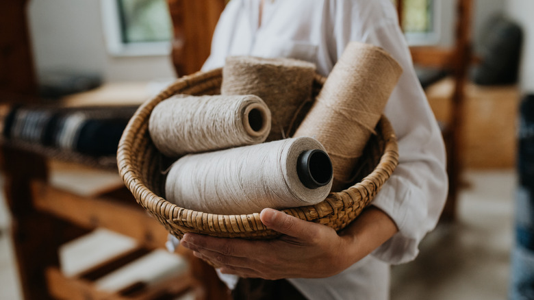 Someone holding a basket full of spools of various material all in beige or neutral colors