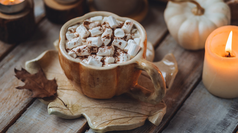 A tea plate shaped like a leaf and a pumpkin shaped cup on top filled with marshmallows and cocoa
