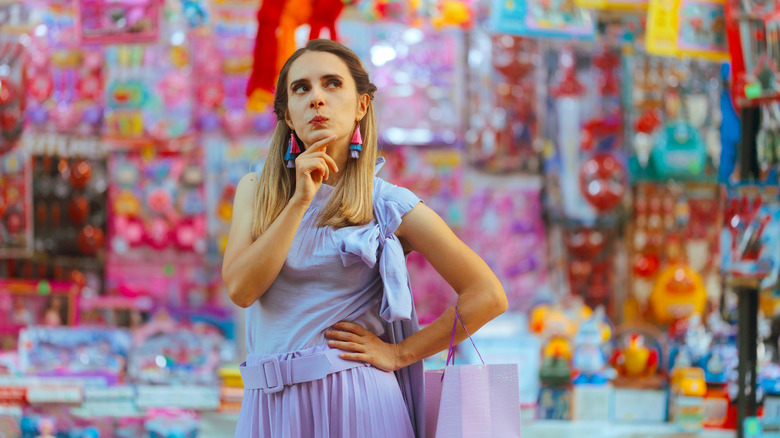 A person standing around surrounded by various items while posed in a thinking position
