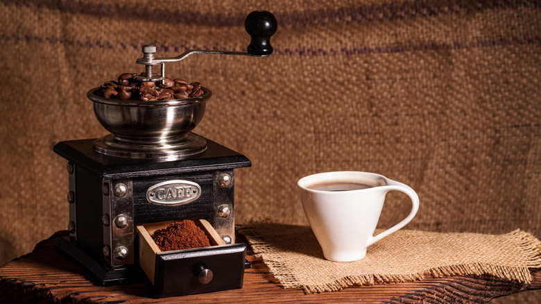 A coffee mill next to a coffee cup.