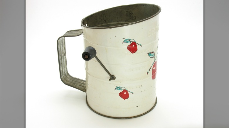 A vintage hand-crank flour sifter with an apple design.