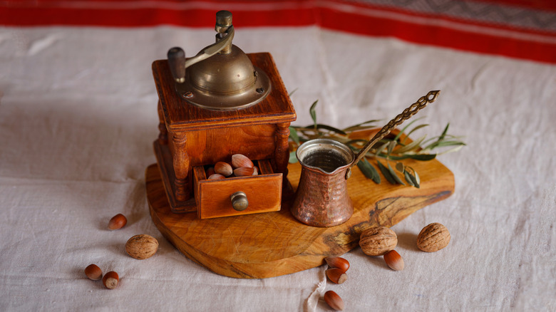 A vintage nut grinder staged with nuts and a tray.