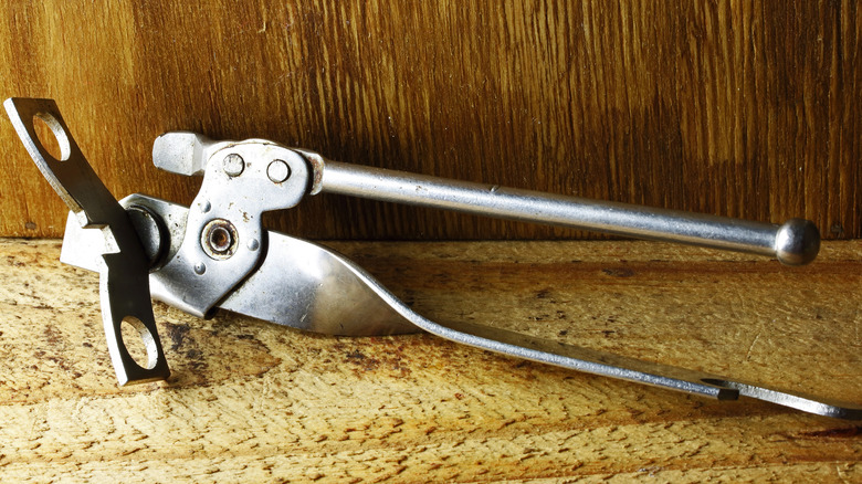 A metal vintage can opener sitting on a wooden shelf.