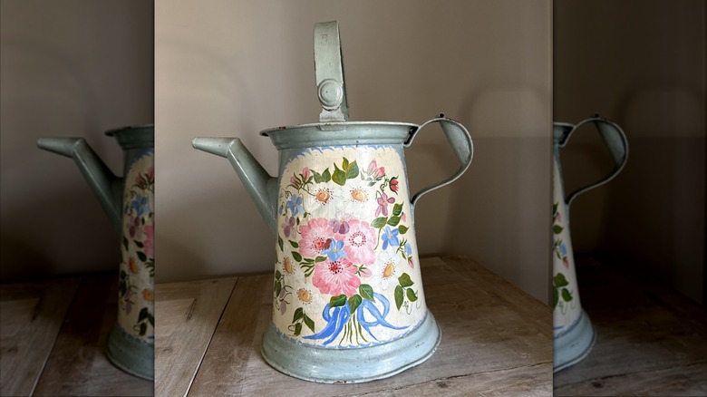 A metal vintage watering can with painted flowers