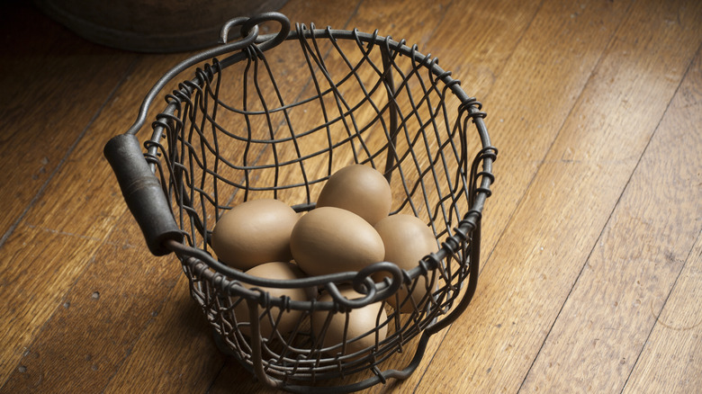 A wire egg basket full of eggs sitting on the floor.