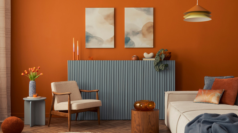 A room with an orange wall, wood floors, tan furniture, and blue accents.