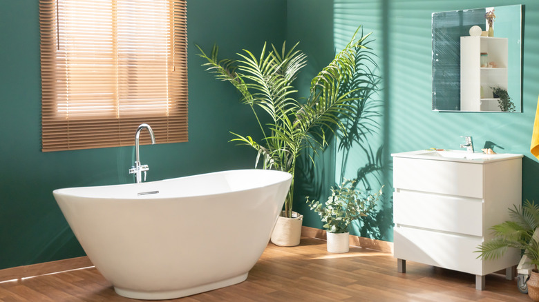 Modern bright bathroom with green walls, wooden floor, plant and window