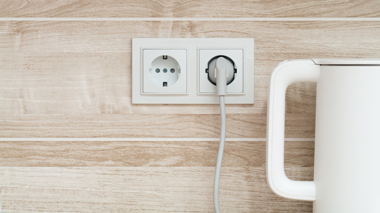 a White electric kettle plugged into a power outlet on a wall in a kitchen