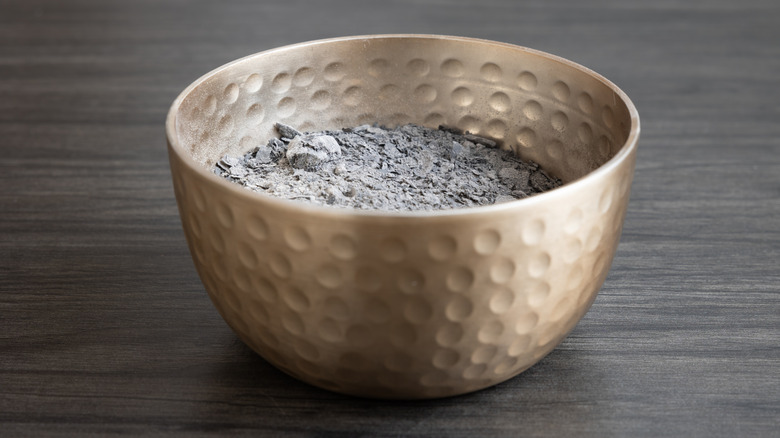 A copper bowl is filled with chunky wood ash