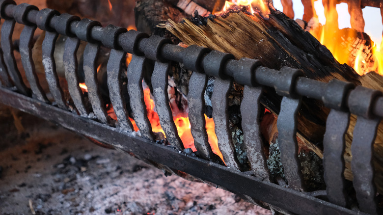 A grate of burning logs is set over a floor of ashes in a fireplace.