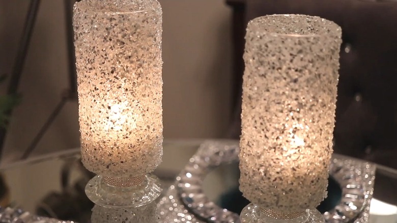 Two candle holders made from vases covered in crushed glass with candles burning inside