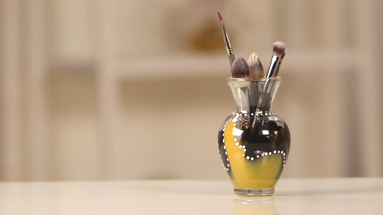 Vase painted black and yellow with white dots holding makeup brushes
