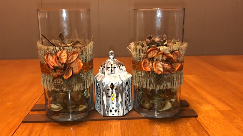 Two tall clear glass vases filled with potpourri and wrapped with ribbon sitting on a table