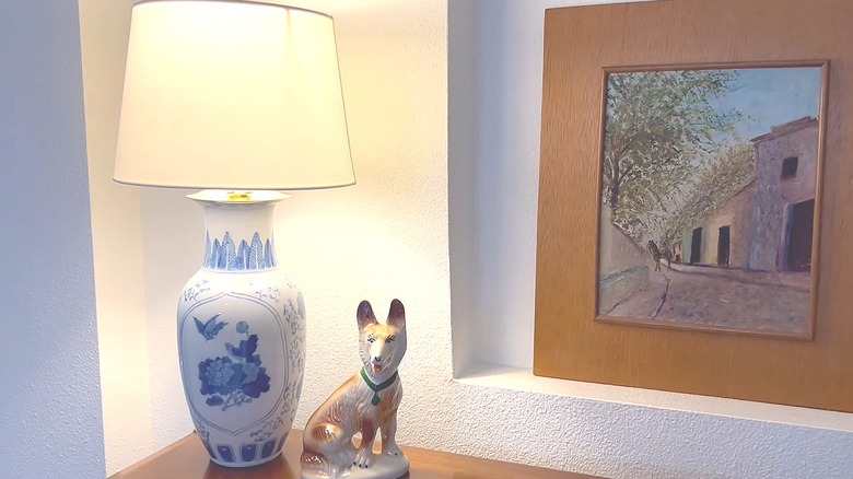 White and blue decorative vase turned into a lamp sitting on a table next to a dog statue and a painting