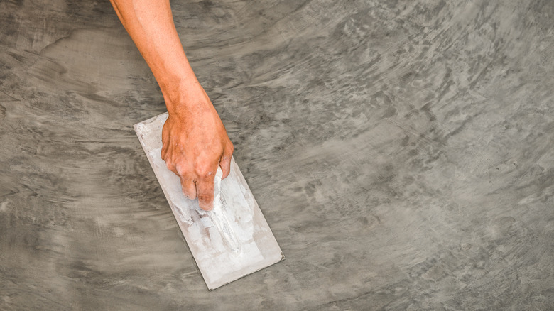 A hand creating a trowel finished concrete slab.