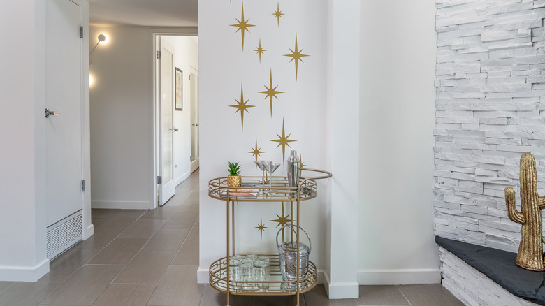 A gold-finished bar cart against a wall with gold starburst accents