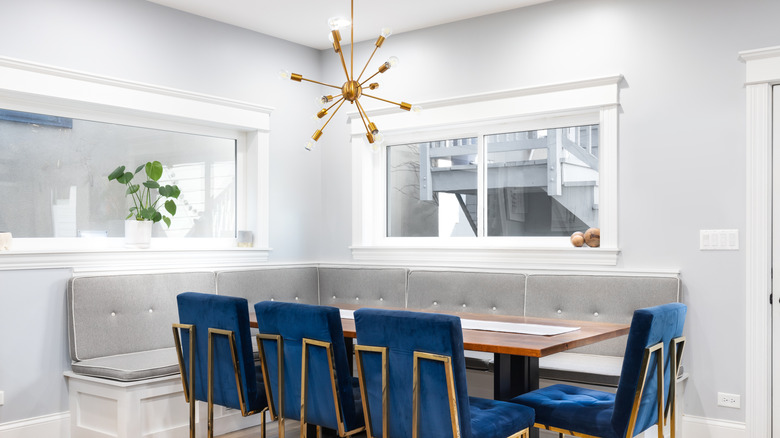 A sputnik chandelier hangs in a white dining room over a banquet with gray cushions and four blue chairs