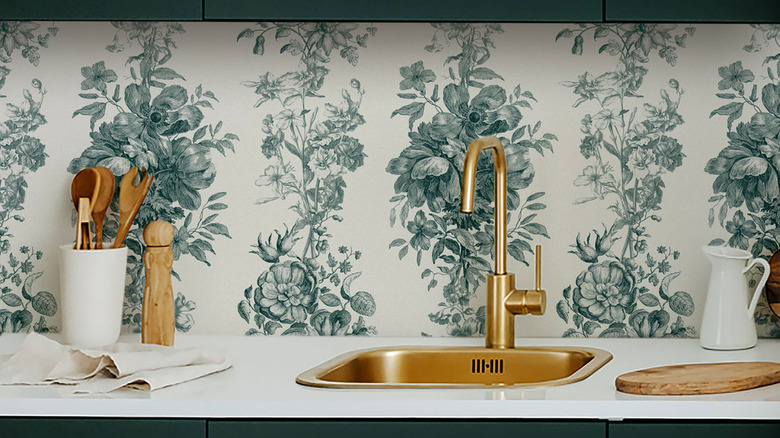 A wallpaper kitchen backsplash and gold sink.