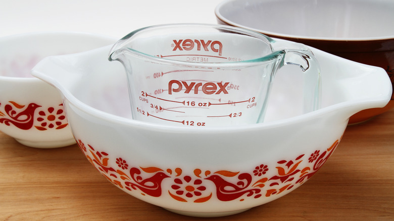 A Pyrex measuring cup sits inside a white and red Pyrex casserole dish.