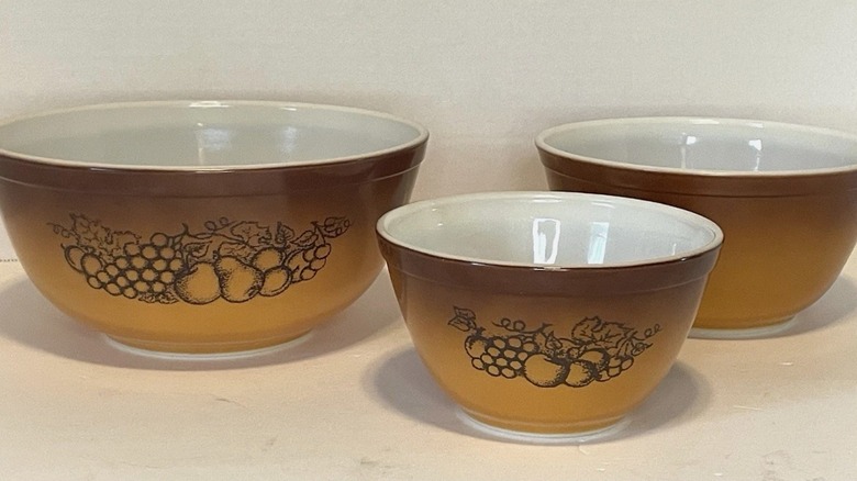 A trio of tan to brown ombre Pyrex bowls decorated with printed fruit