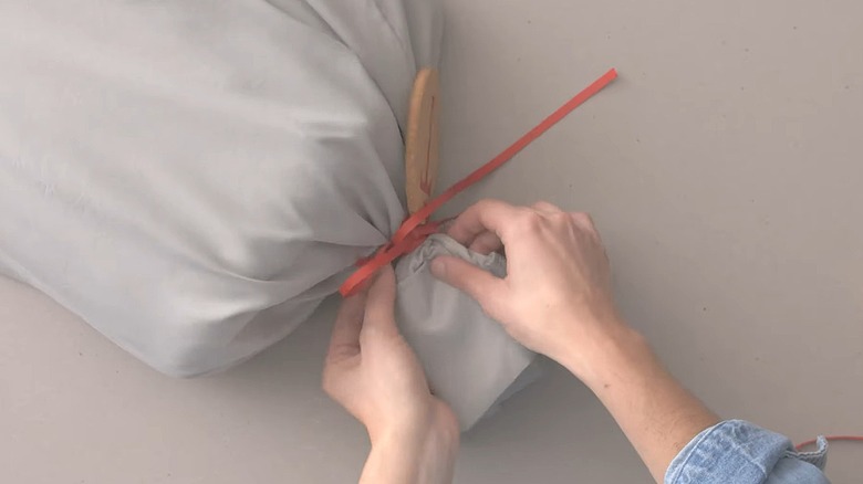 Person tying the top of a pillowcase closed with a present inside