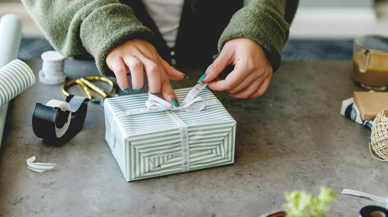 Person wearing a sweater and wrapping presents with tape and scissors nearby