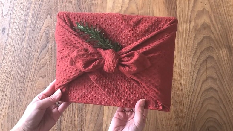 Small gift wrapped in a burgundy textured towel with a sprig of pine in it