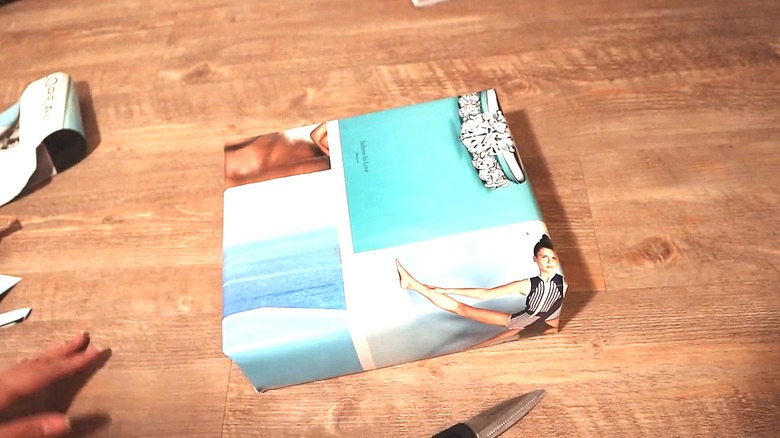 Present wrapped in magazine pages on a table next to scraps and a pen