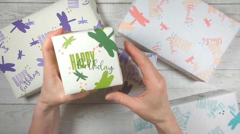 Multiple presents wrapped in white paper stamped in multicolored dragonfly designs and words