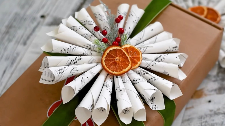 Gift with sheet music, orange slices, berries, and pine decorating the top