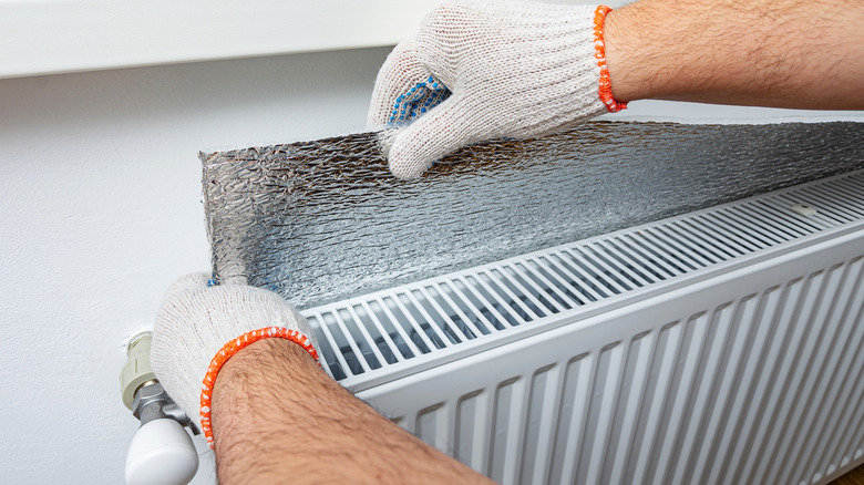 Gloved hands place aluminum foil behind a radiator.
