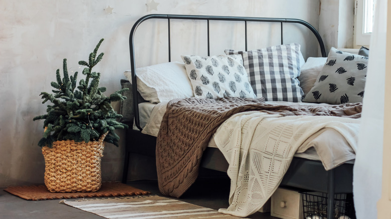 A bed near a window with knitted blankets and a houseplant.