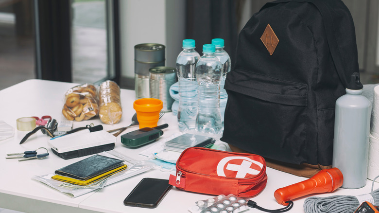A backpack on a table surrounded by survival kit supplies.